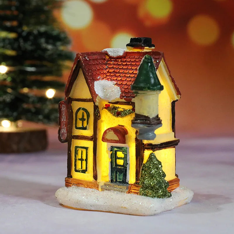 A miniature festive Christmas house with a tiled roof and warm LED light glow, resting on a snowy base.