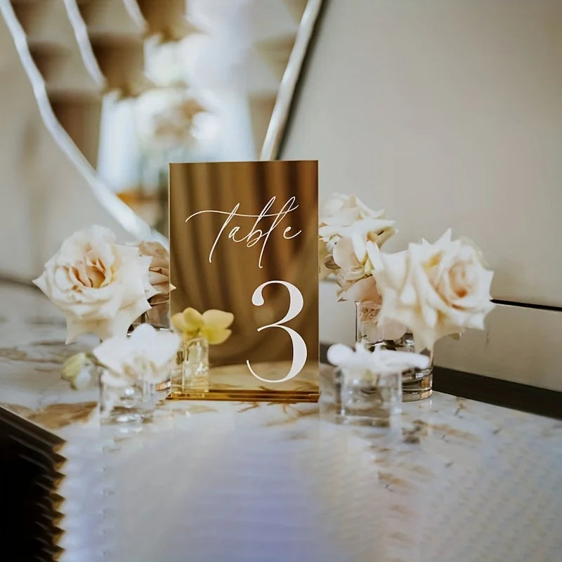 Elegant gold plated mirrored acrylic table numbers with the number three and white roses on a table.