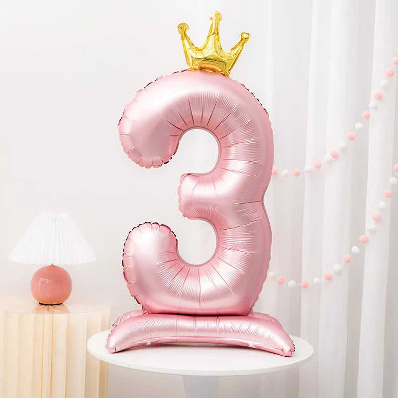 A pink foil balloon shaped like the number three with a gold crown on top