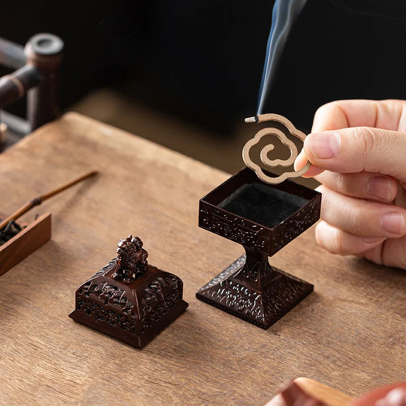 A hand holds a dark brown Chinoiserie Square Pixiu incense burner with smoke rising from it on a wooden surface.
