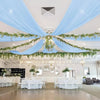 Light blue sheer chiffon curtains draped across a ceiling with greenery for an event venue