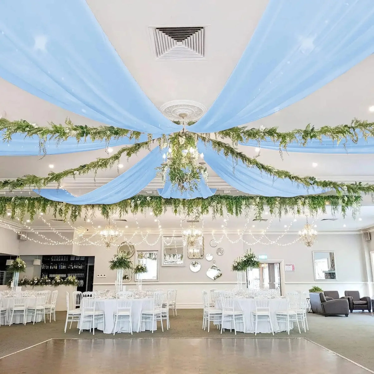 Light blue sheer chiffon curtains draped across a ceiling with greenery for an event venue