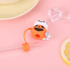 Orange silicone straw covers with white silicone lids and a clear glass cube on a pink background