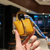 A hand holds a yellow mini handbag with a blue patterned wrist strap against a blurred indoor background.