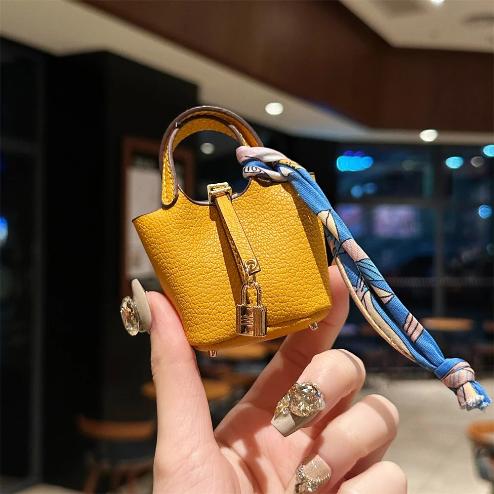 A hand holds a yellow mini handbag with a blue patterned wrist strap against a blurred indoor background.