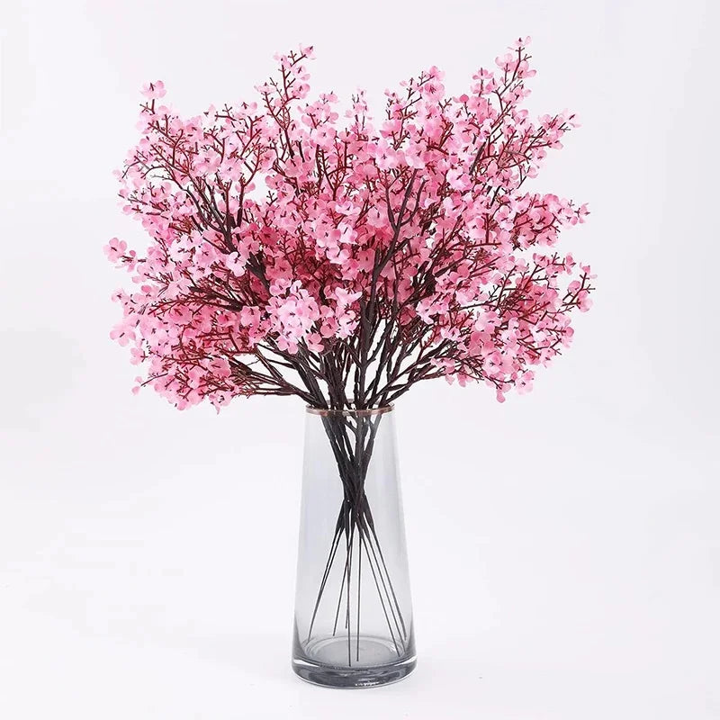 A bouquet of pink cherry blossom and gypsophila artificial flowers displayed in a clear glass vase.