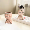 A terracotta resin girl face planter with painted features and a brush holder sits on a white surface.
