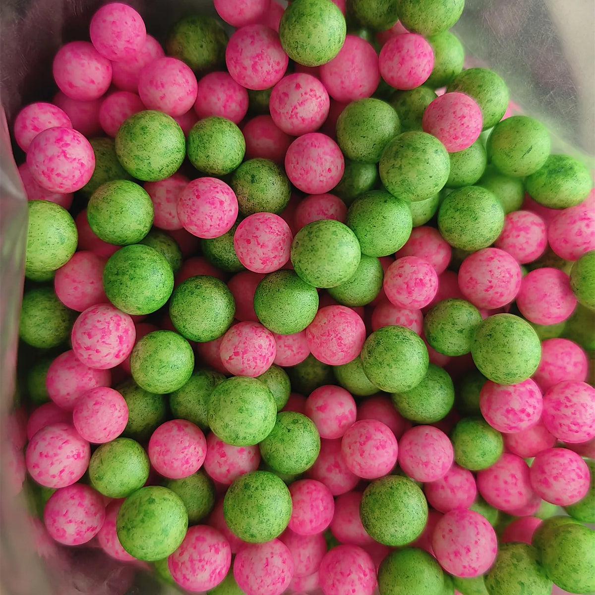 A close-up view of pink and green foam beads scattered in a translucent container.