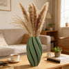 A tall vase filled with dried pampas grass sits on a wooden table in a minimalist living room setting.