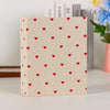 A square beige photo album with a repeating pattern of small red hearts on the cover.