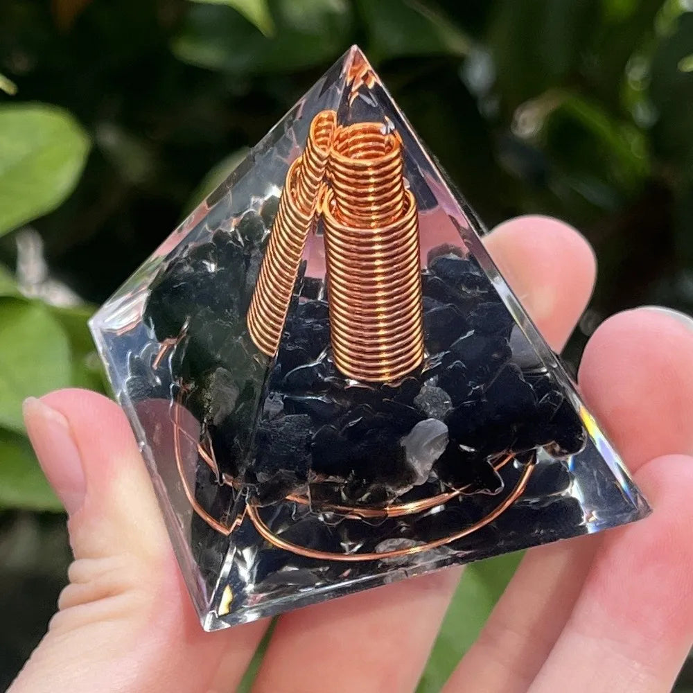 Handmade resin orgonite pyramid with natural obsidian and copper coil held in a hand