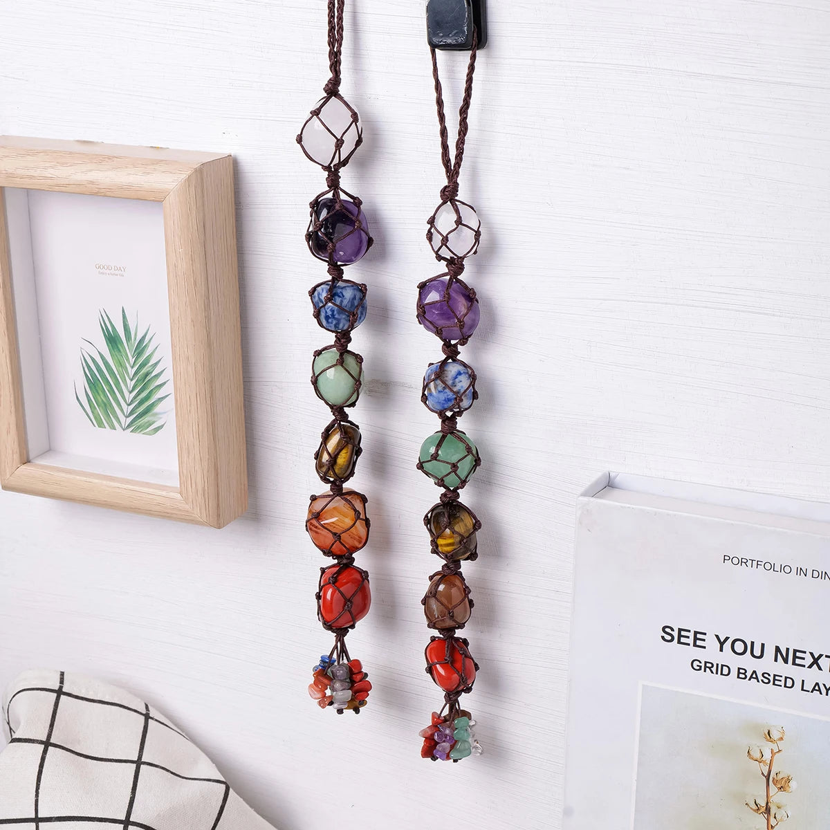 A pair of natural crystal chakra rolling stone pendants hanging on a white wall.