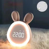 A pink bunny-shaped mini LED cartoon alarm clock night light glowing brightly on a fluffy surface.