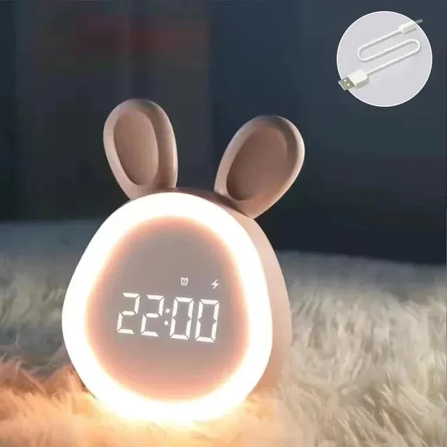 A pink bunny-shaped mini LED cartoon alarm clock night light glowing brightly on a fluffy surface.