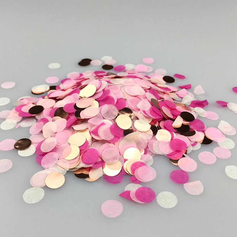 A pile of multicolor paper confetti consisting of pink, gold, and black circular pieces scattered on a light gray surface.