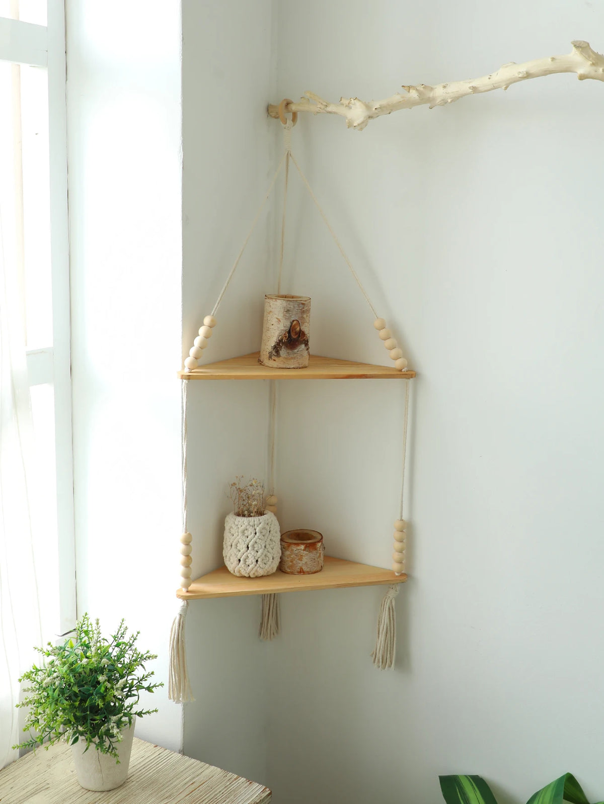 Étagère flottante en bois bohème affichant des éléments naturels comme du bois et de la mousse sur un mur blanc.