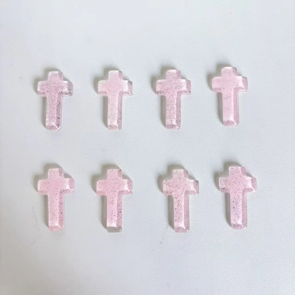 Ein Set aus fünf rosa glitzernden Kristallkreuzdekorationen in einer Reihe angeordnet.