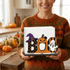 A woman holds a wooden tissue dispenser featuring a carved pumpkin and ghost design against an orange sweater.