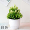 Un pot de bonsaï artificiel avec un feuillage vert vif et des fleurs blanches repose sur une surface claire.