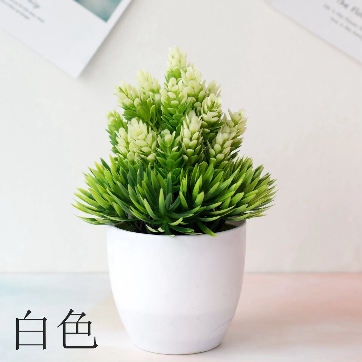 Un pot de bonsaï artificiel avec un feuillage vert vif et des fleurs blanches repose sur une surface claire.