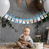 A baby sitting on a rug in front of a decorative banner marking months for a first birthday growth record.