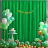 A vibrant green satin backdrop curtain decorated with balloons, a cake, and gold accents for a birthday party.