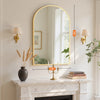 A gold-framed arched mirror hangs above a marble mantelpiece with decorative lamps and a thermometer.