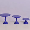 Three purple metal cake stands with pedestal bases displayed on a white surface.