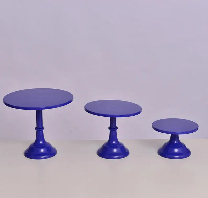 Three purple metal cake stands with pedestal bases displayed on a white surface.