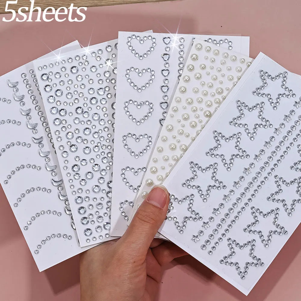 A hand holds several sheets of glitter gem stick-on facial tattoos featuring various heart and star patterns.