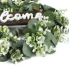 Artificial eucalyptus greenery with a wooden welcome sign on a white background.