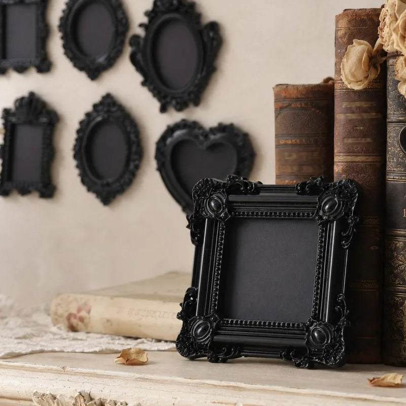 A collection of black vintage resin mini picture frames displayed on a light wooden surface next to stacked old books.