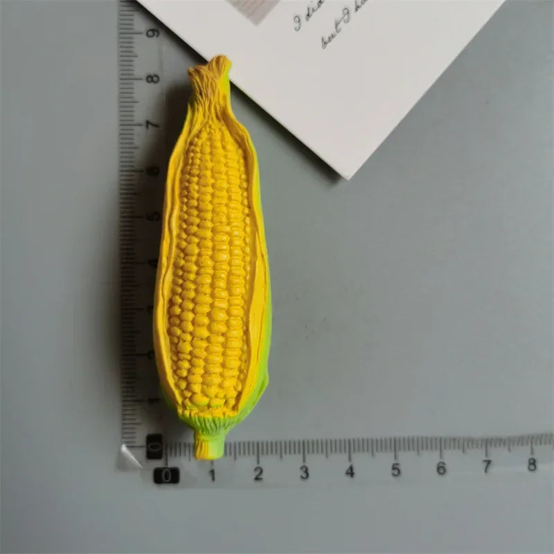 A bright yellow corn on the cob is positioned next to a ruler and a piece of paper.