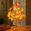 An LED maple leaf table lamp with warm glow illuminates autumn leaves against a window blind.