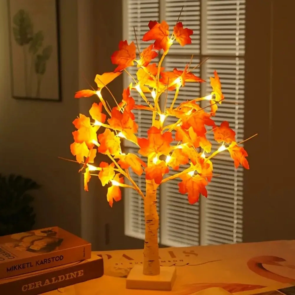 An LED maple leaf table lamp with warm glow illuminates autumn leaves against a window blind.