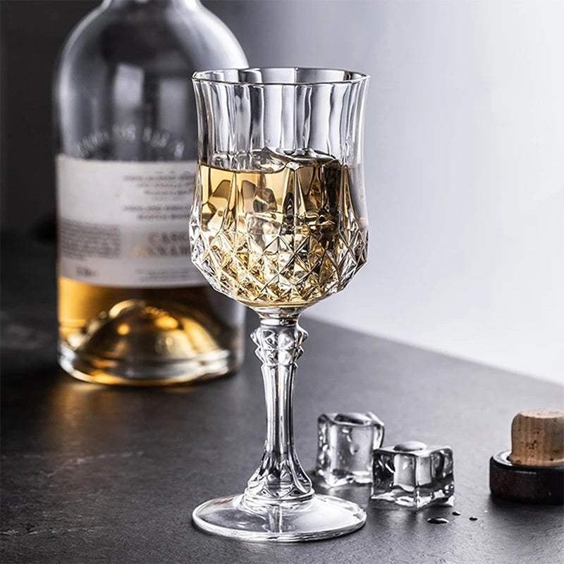 A clear glass of golden wine sits next to a bottle and a set of reusable plastic wine glasses.