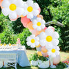 A large balloon arch featuring white and yellow daisy balloons set up outdoors on a grassy area.