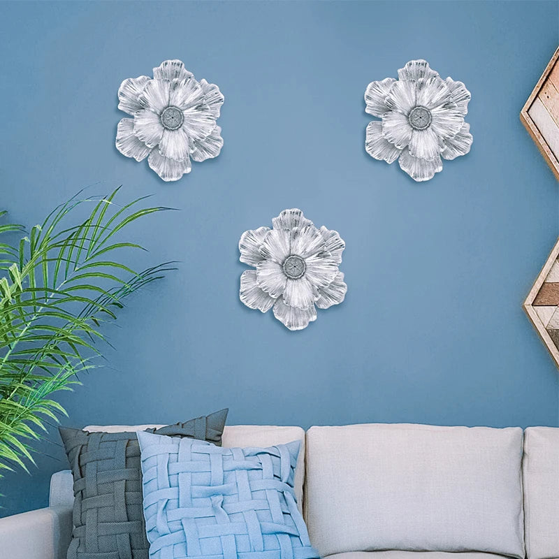 Three white flower-shaped resin wall art pieces displayed on a blue wall above a light sofa.