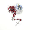 A set of red wood beads and a silver crucifix necklace displayed next to a clear container with a religious image.
