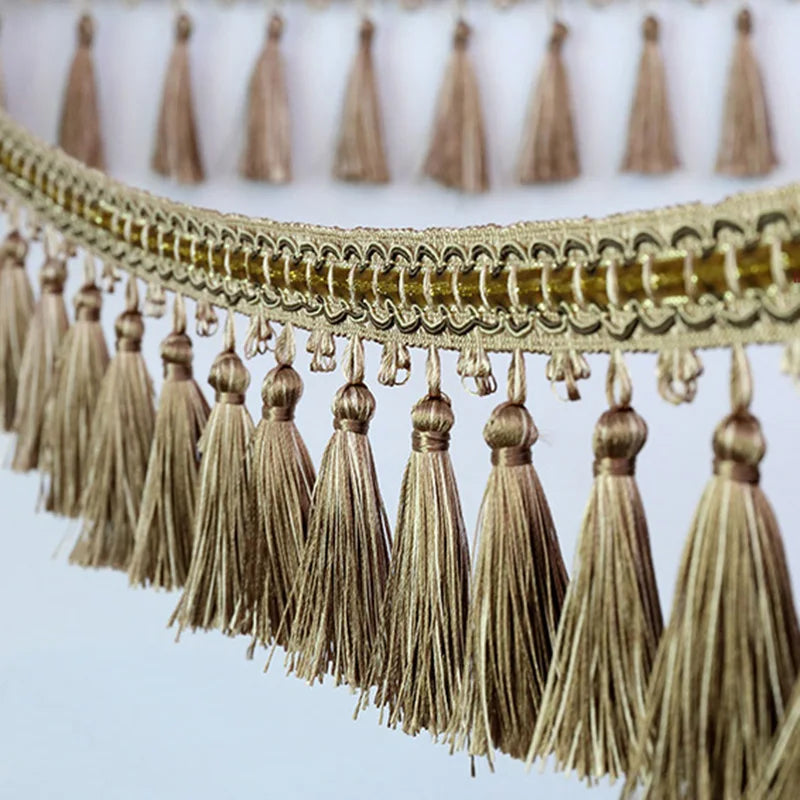 Golden decorative tassel fringe trim with a beige border and multiple tassels hanging from it.