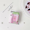 A pink plastic milk bottle photo keychain with a strawberry design and a silver clasp is shown on a white surface.