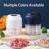 A white electric food chopper is shown next to a blue one, with chopped pink ingredients on a wooden board.