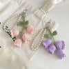 Handmade crocheted flower keyrings in pink and purple colors displayed on a white fabric bag.