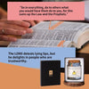 A black jar labeled with a gold cross sits on a wooden surface next to an open Bible.