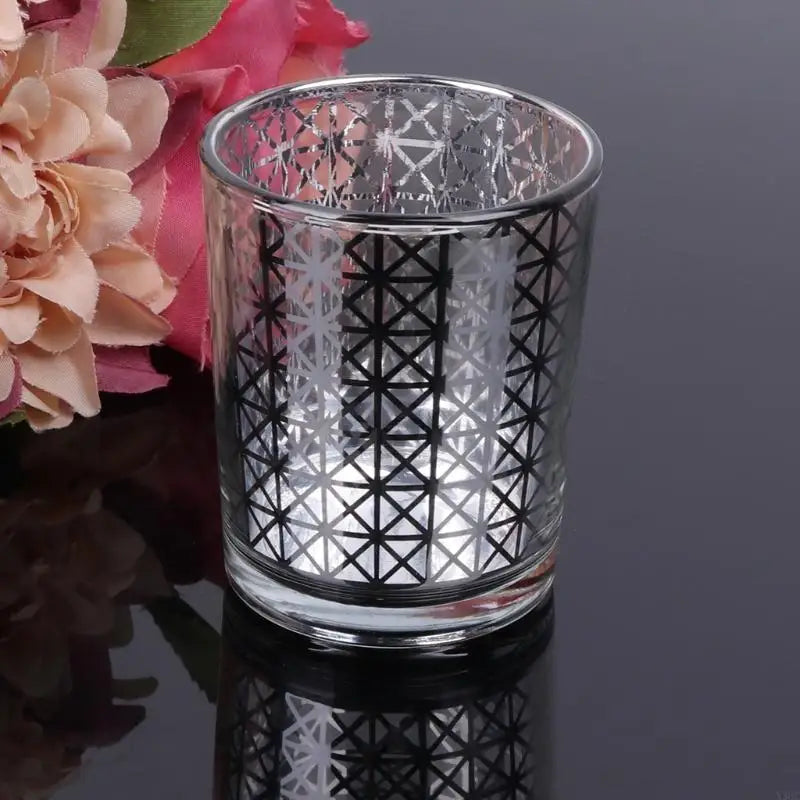 Elegant glass votive candle holder with a geometric cut pattern and a floral decoration.