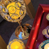 A golden crystal candle holder with a yellow flame sits on a red tray, decorated with purple and teal accents.