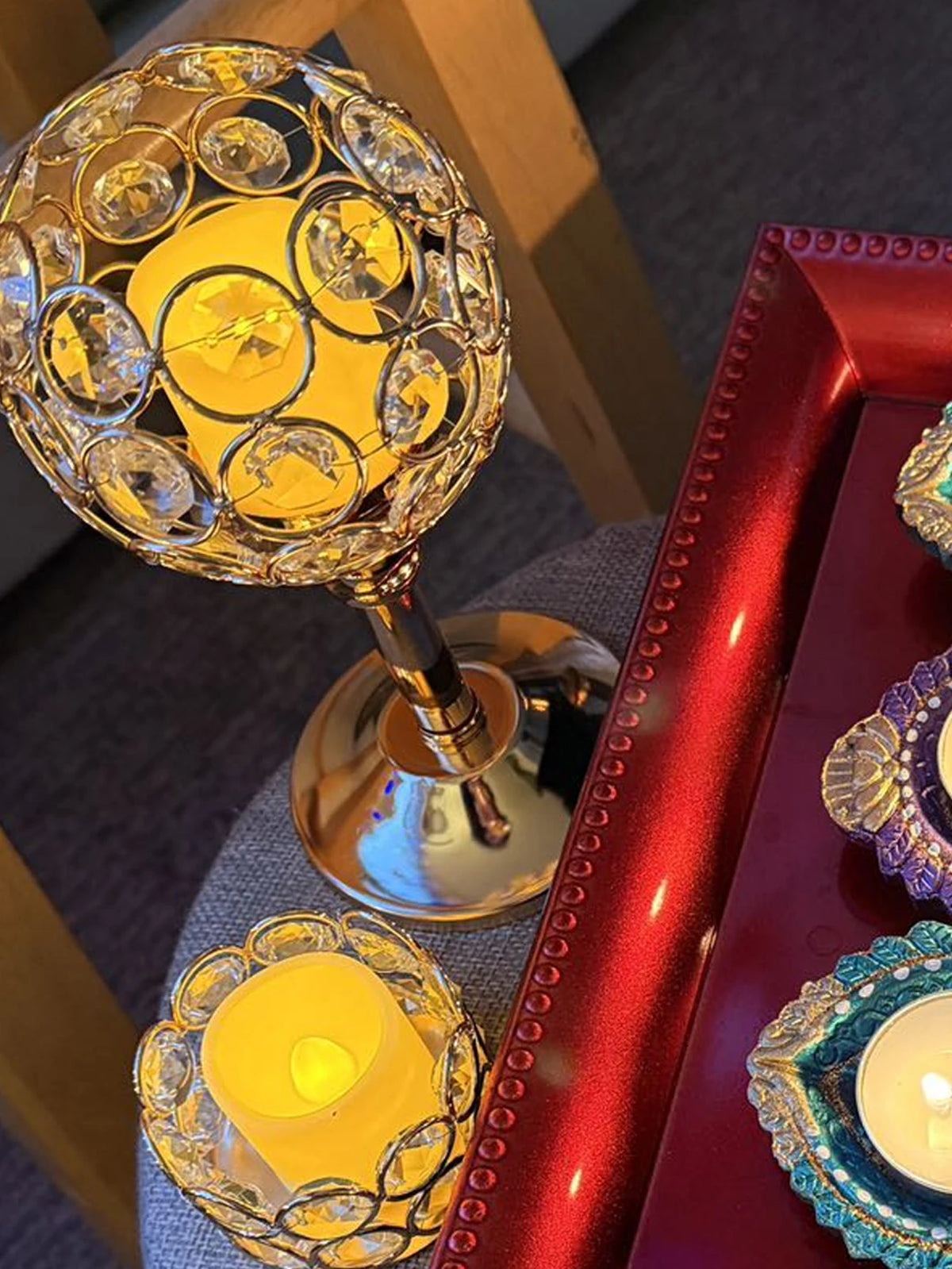 A golden crystal candle holder with a yellow flame sits on a red tray, decorated with purple and teal accents.