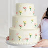 A three-tiered white cake decorated with pink and yellow roses, held by a person.