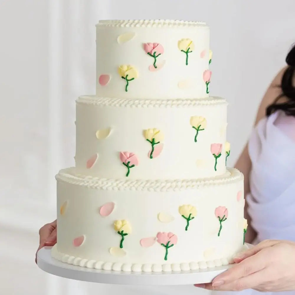 A three-tiered white cake decorated with pink and yellow roses, held by a person.