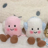 A set of two fluffy marshmallow plush toys, one pink and one white, resting on a white surface.
